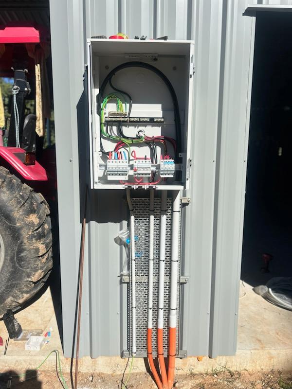 Completed shed power distribution board with safety switches and underground cable entries on a metal workshop wall