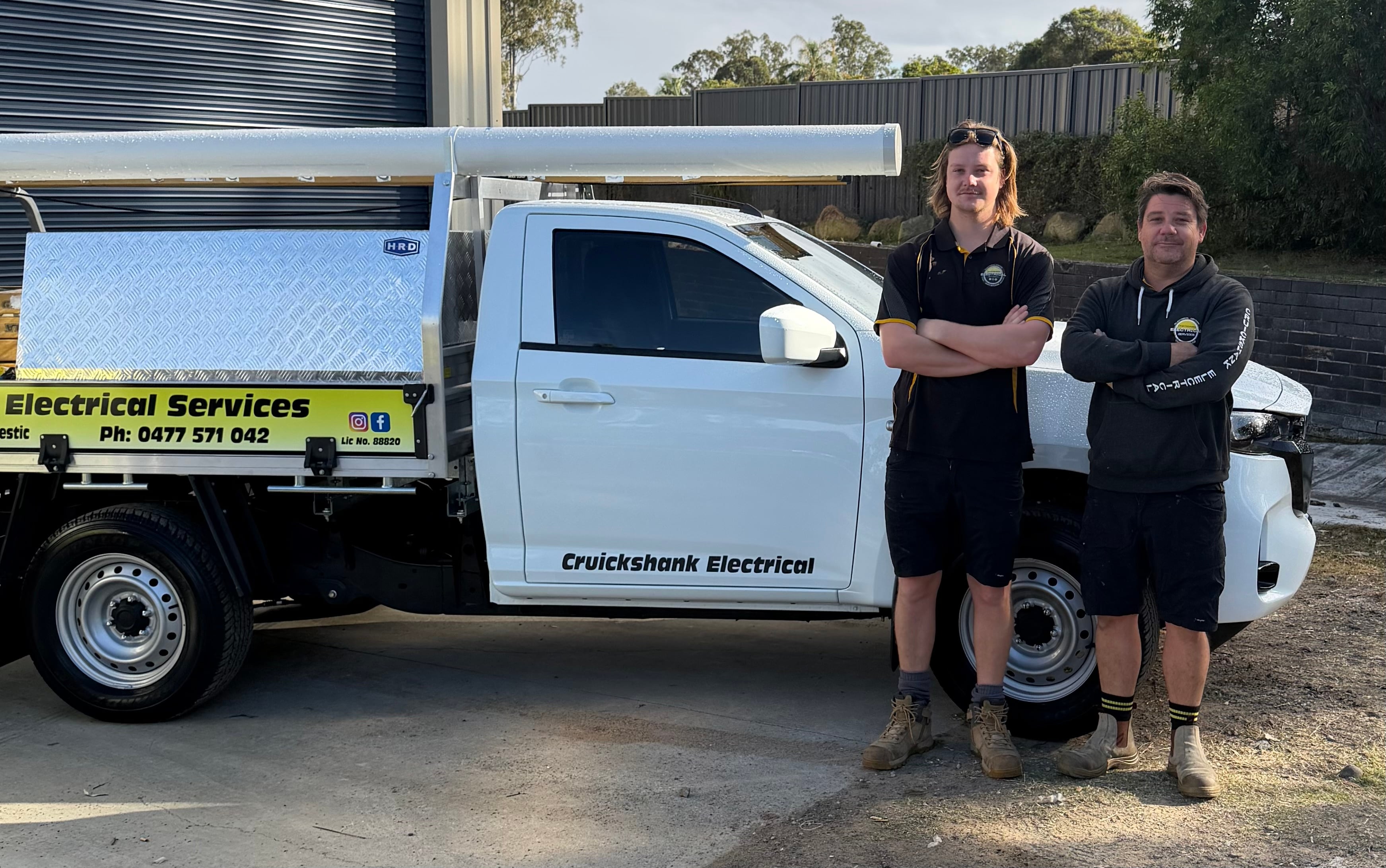 Two Cruickshank Electrical team members standing beside their white work ute