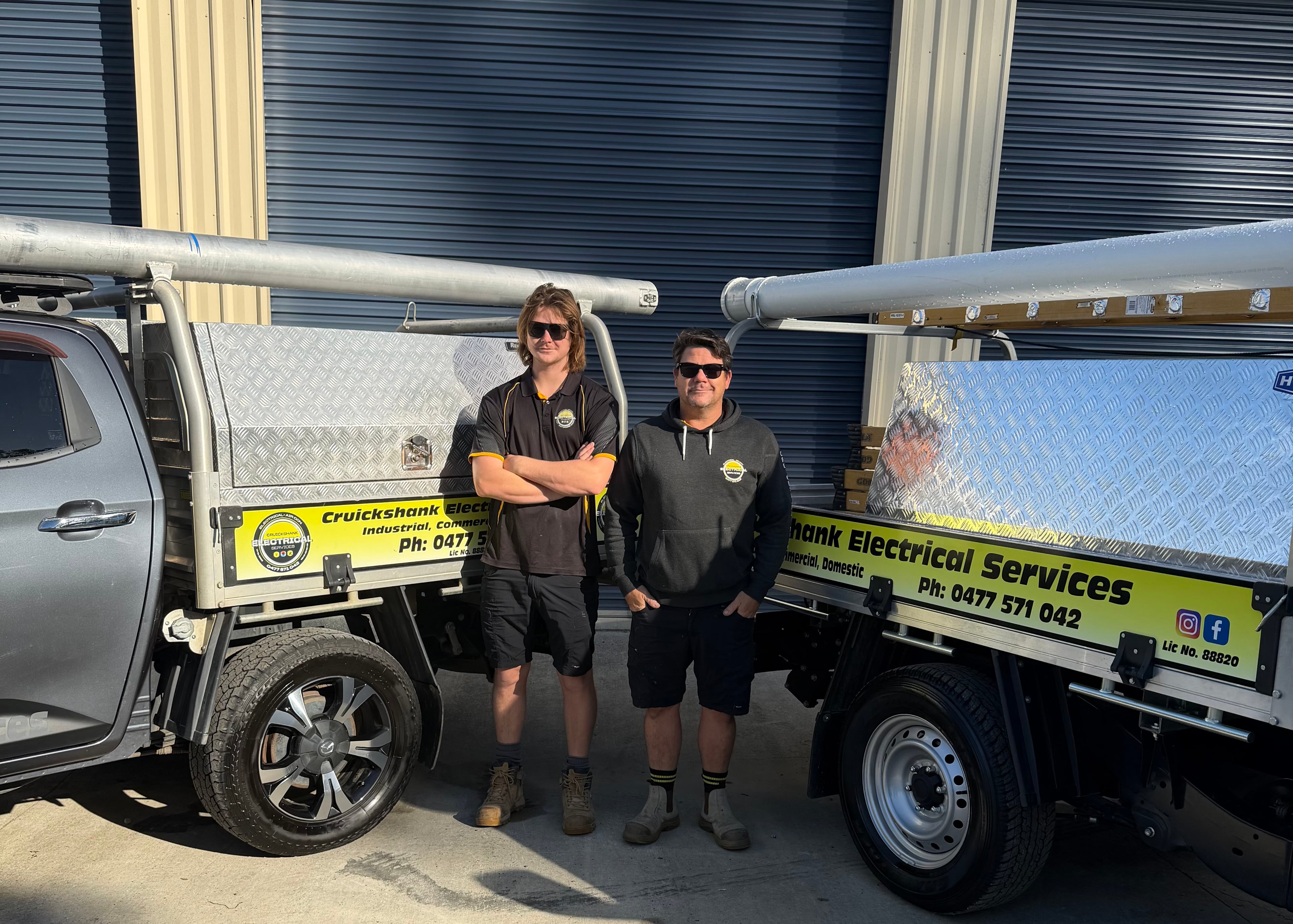 The Cruickshank Electrical team standing together between their two branded work utes